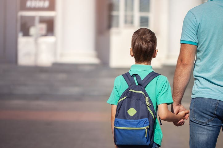 Dads on Duty - Father leads a little child school boy go hand in hand. Parent and son with backpack behind the back