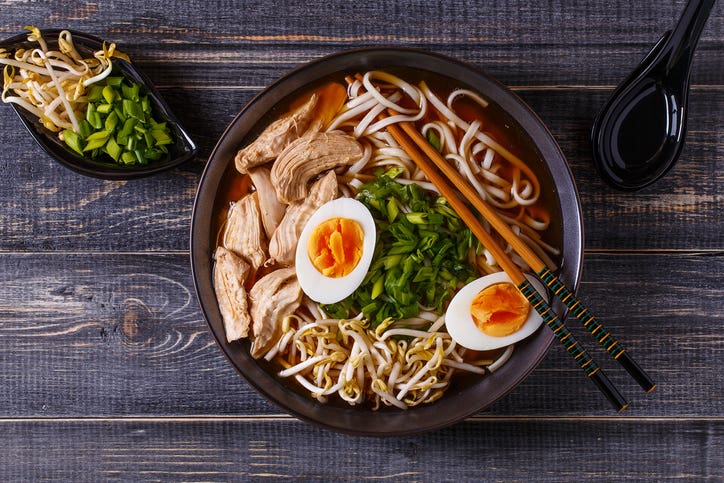 Japanese ramen soup with chicken, egg, chives and sprout on dark wooden background.