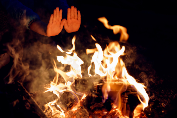 Child's hands stretched to burning campfire at night. Warming palms at fire. - camp craft and vine